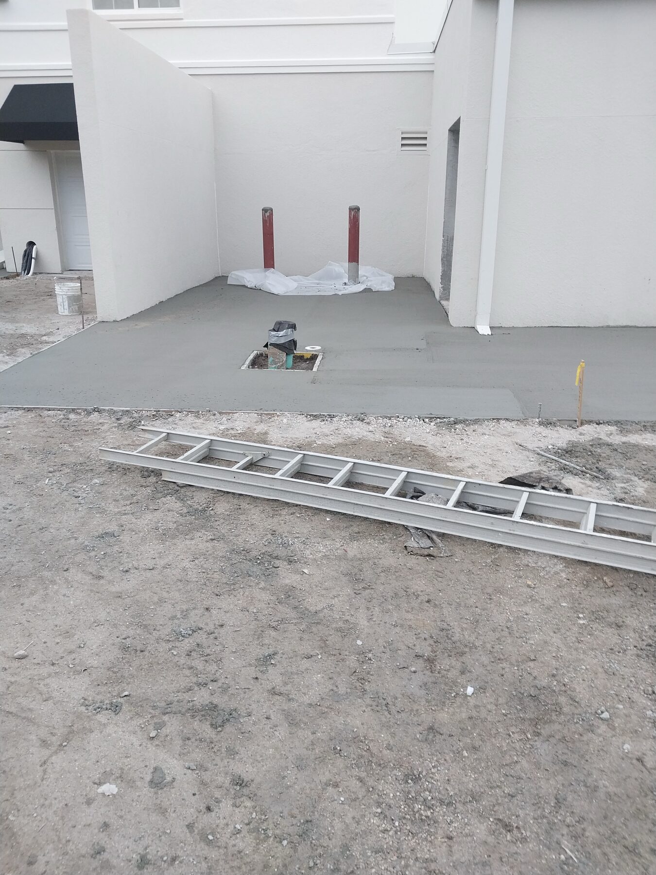 Newly poured commercial concrete entry pad with red protective bollards in front of a hotel service entrance