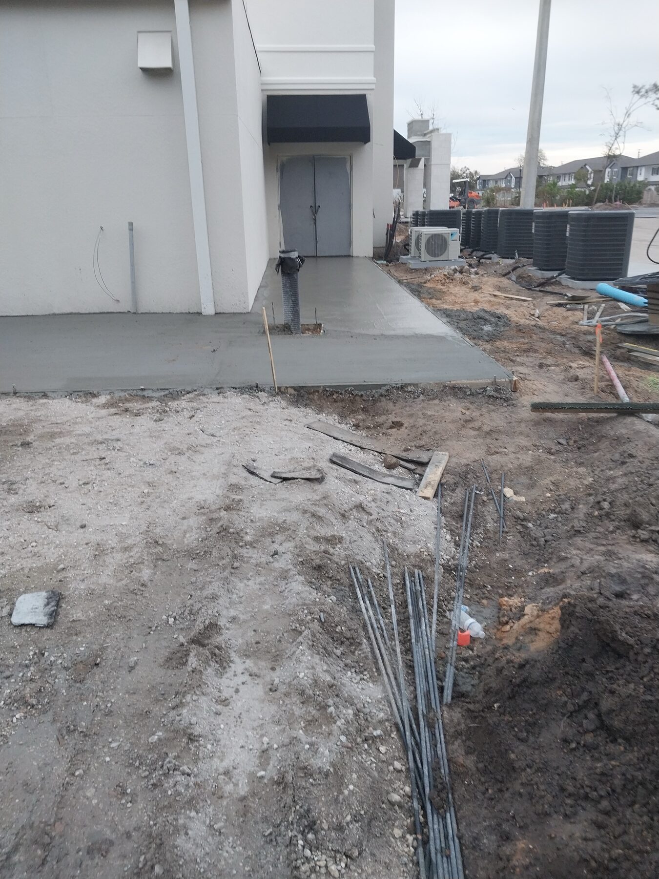 Freshly poured commercial concrete approach pad at a rear hotel entry door, with rebar and prep work for the next section visible