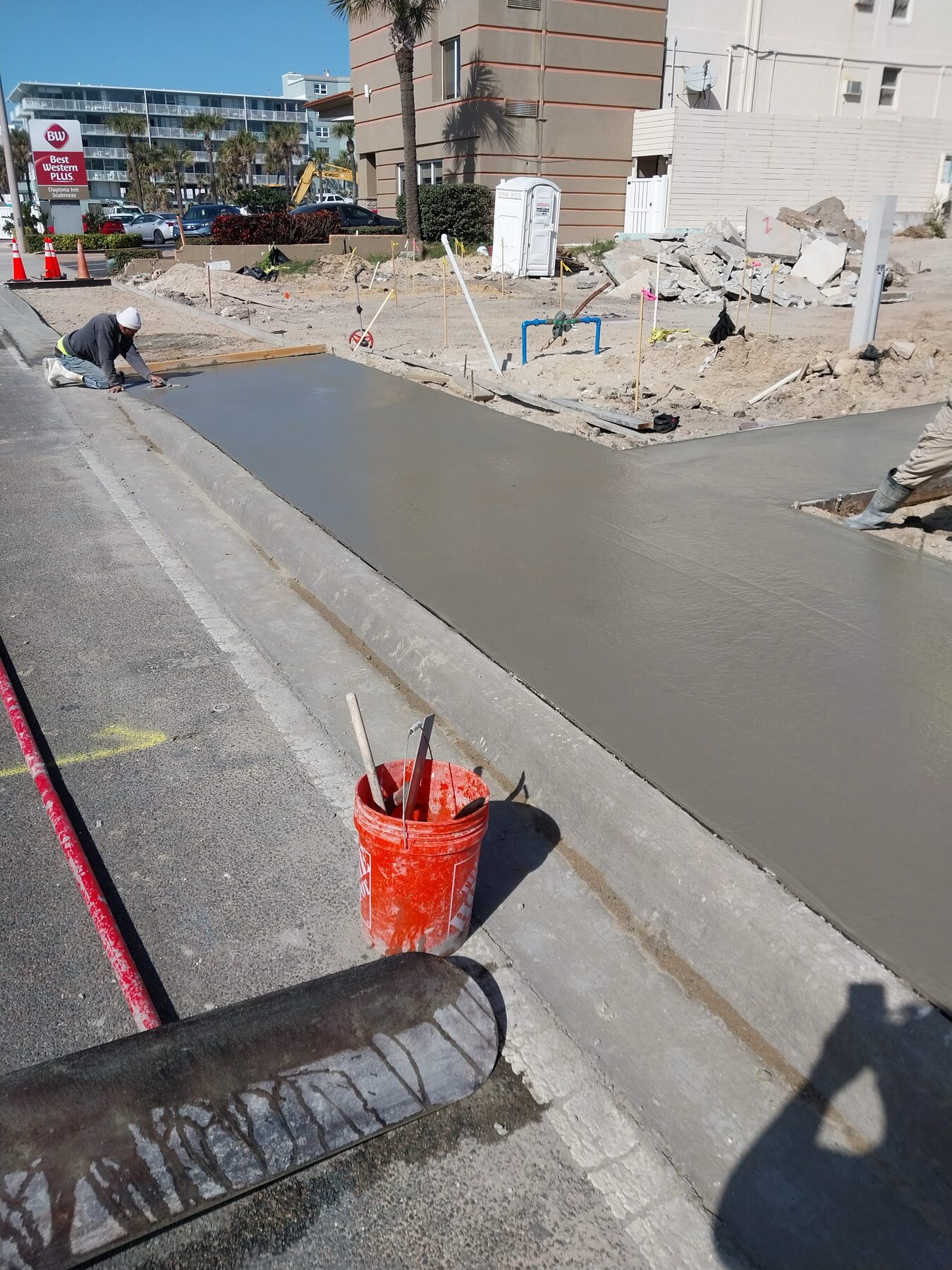 Crew finishing a freshly poured commercial concrete sidewalk in front of a Daytona Beach hotel