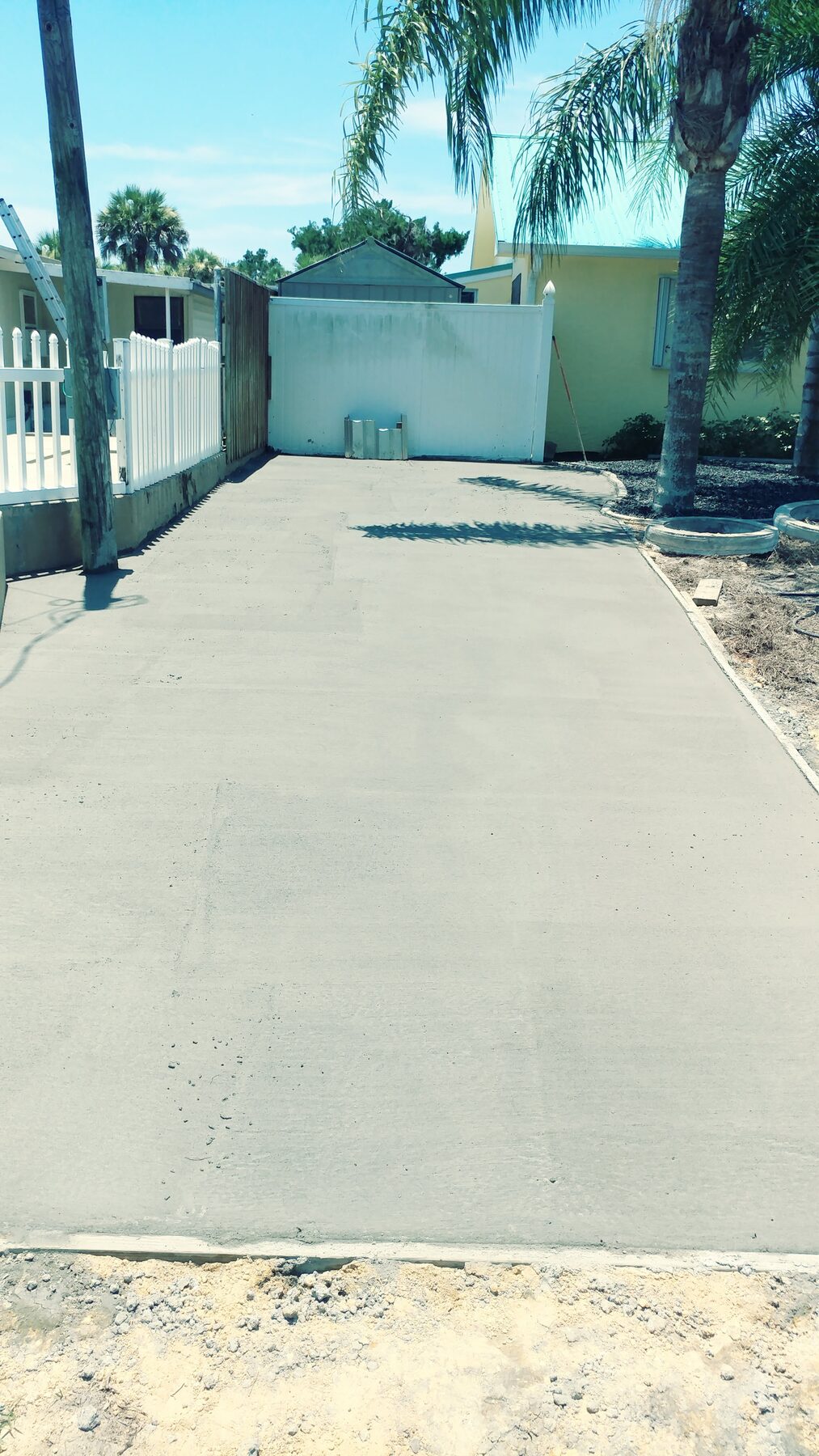 Finished long residential concrete driveway between a house and white vinyl fence in Central Florida