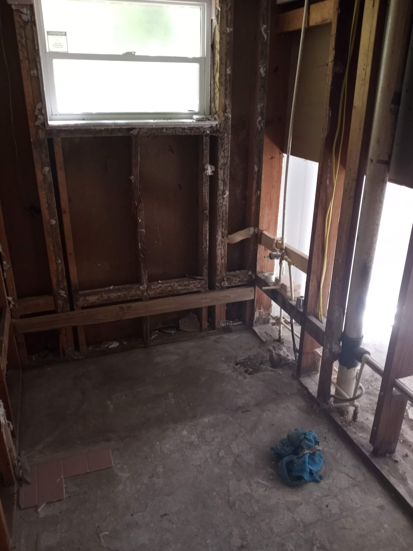 Bathroom fully gutted to wall studs and concrete subfloor with rough plumbing exposed and ready for new installation