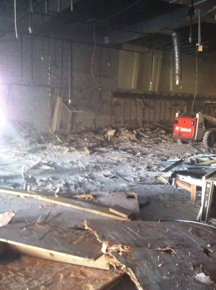 Commercial interior space mid-demolition with Bobcat skid steer working through stacked debris and pulled ceiling grid