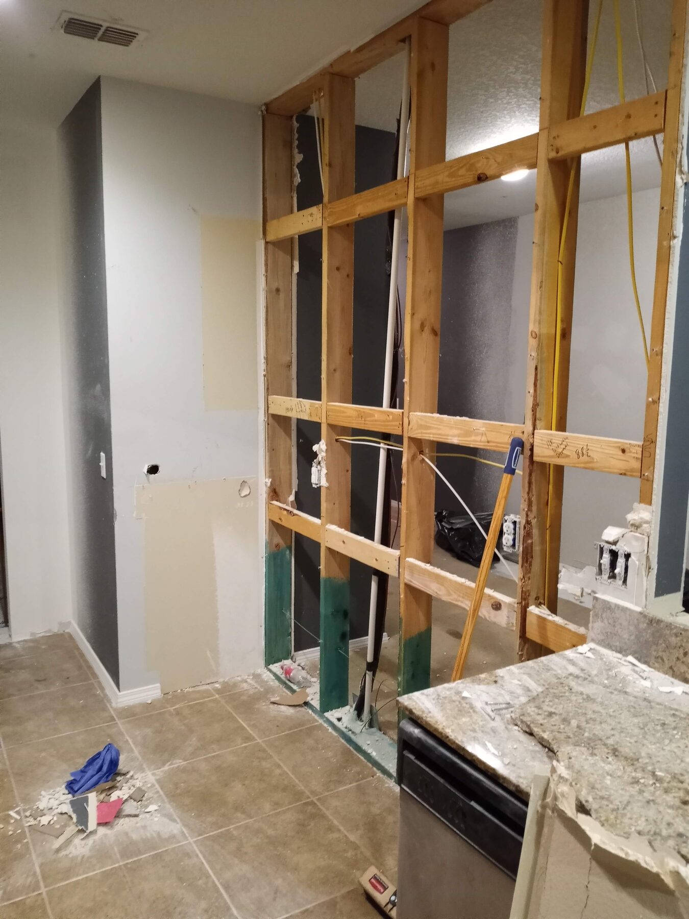Kitchen during selective demolition with drywall removed, exposing wall studs and rough plumbing