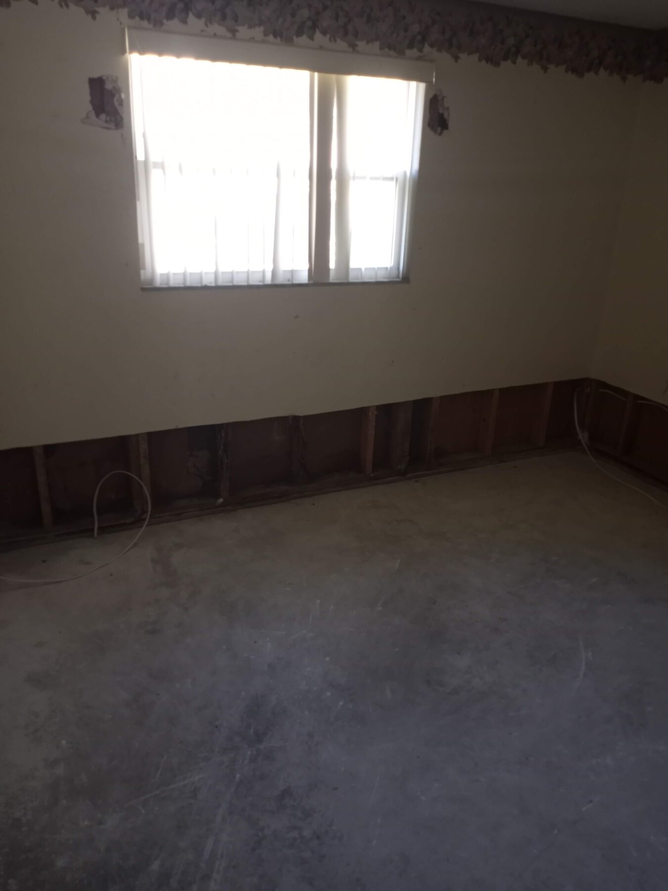 Bedroom with bottom two feet of drywall and baseboards removed for water damage remediation, exposing wall framing