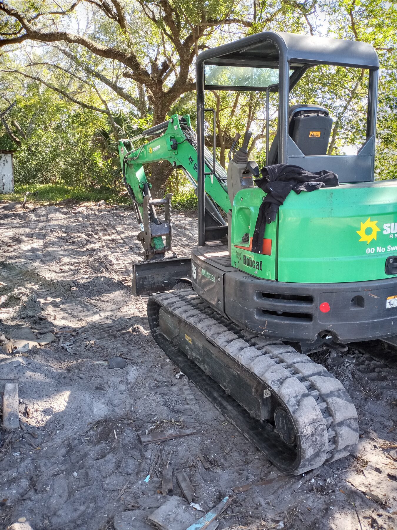 Cleared residential lot after demolition with mini-excavator on graded soil, structure fully removed
