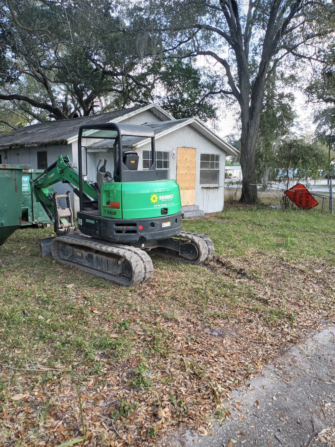 Single-story residential house before demolition with mini-excavator parked beside it ready to begin teardown