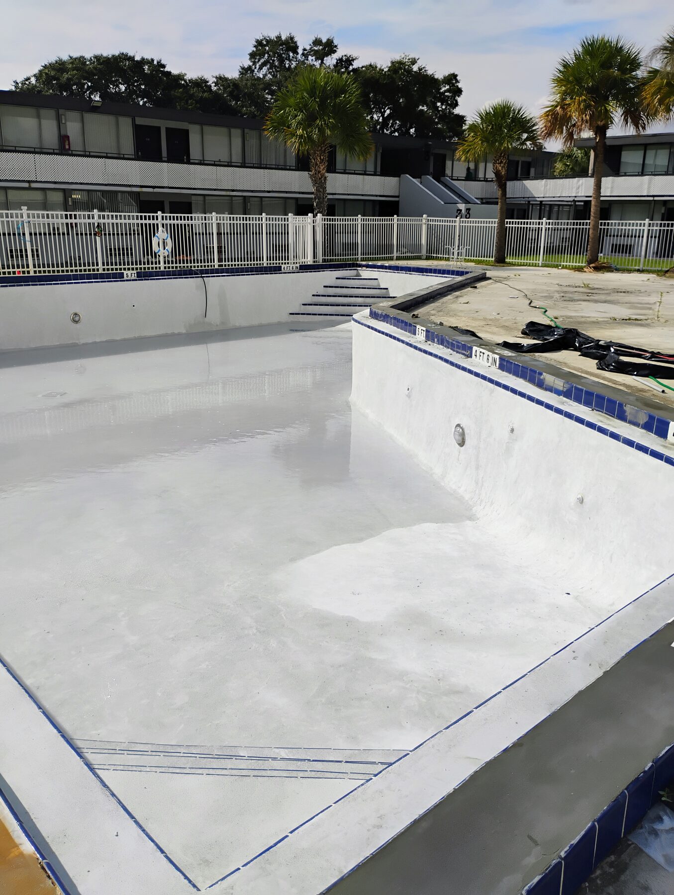 Wide view of finished commercial pool plastering job in Central Florida — new white plaster and blue tile