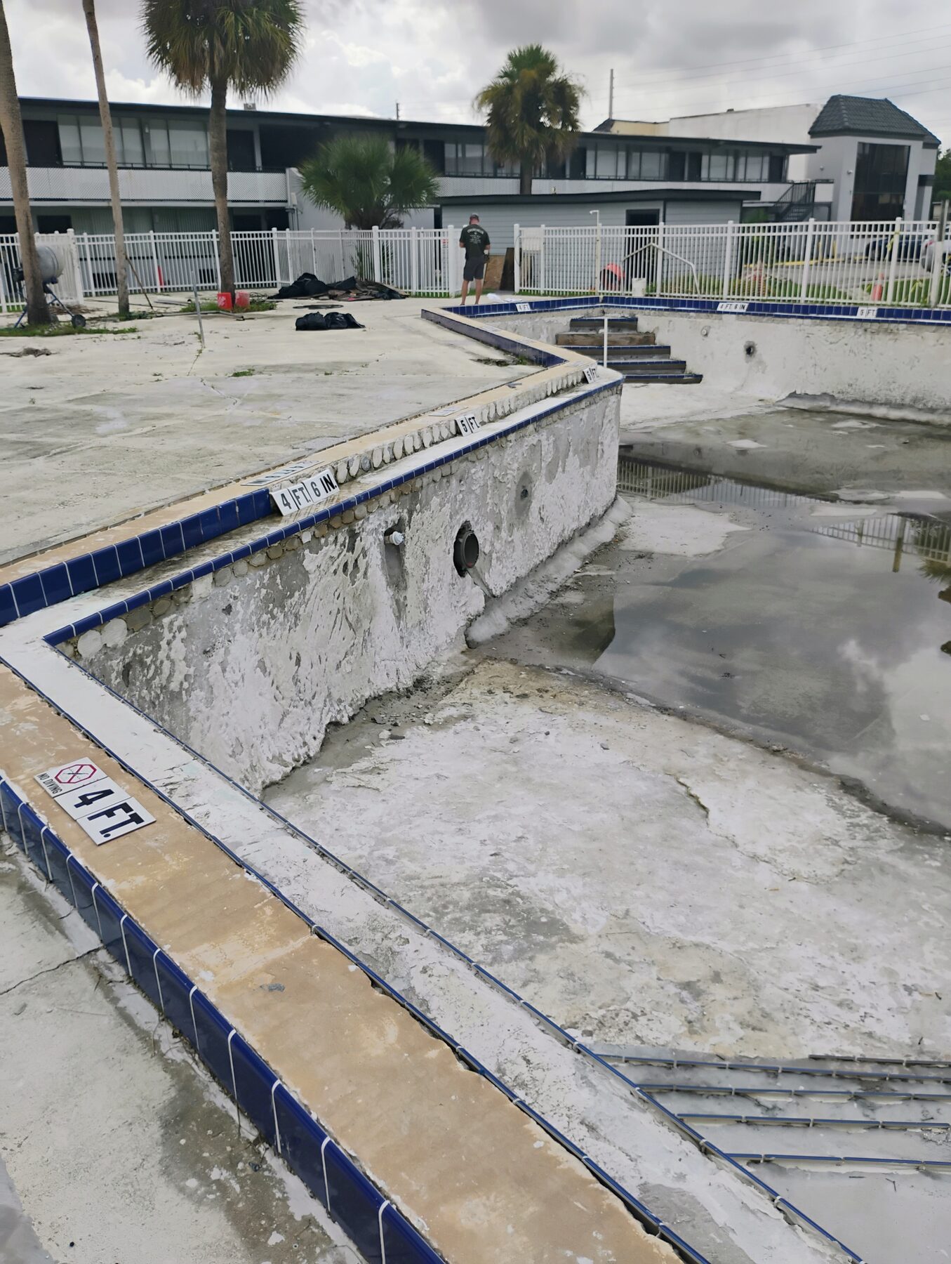 Commercial pool during chip-out — old plaster removed, substrate exposed, new coping in place