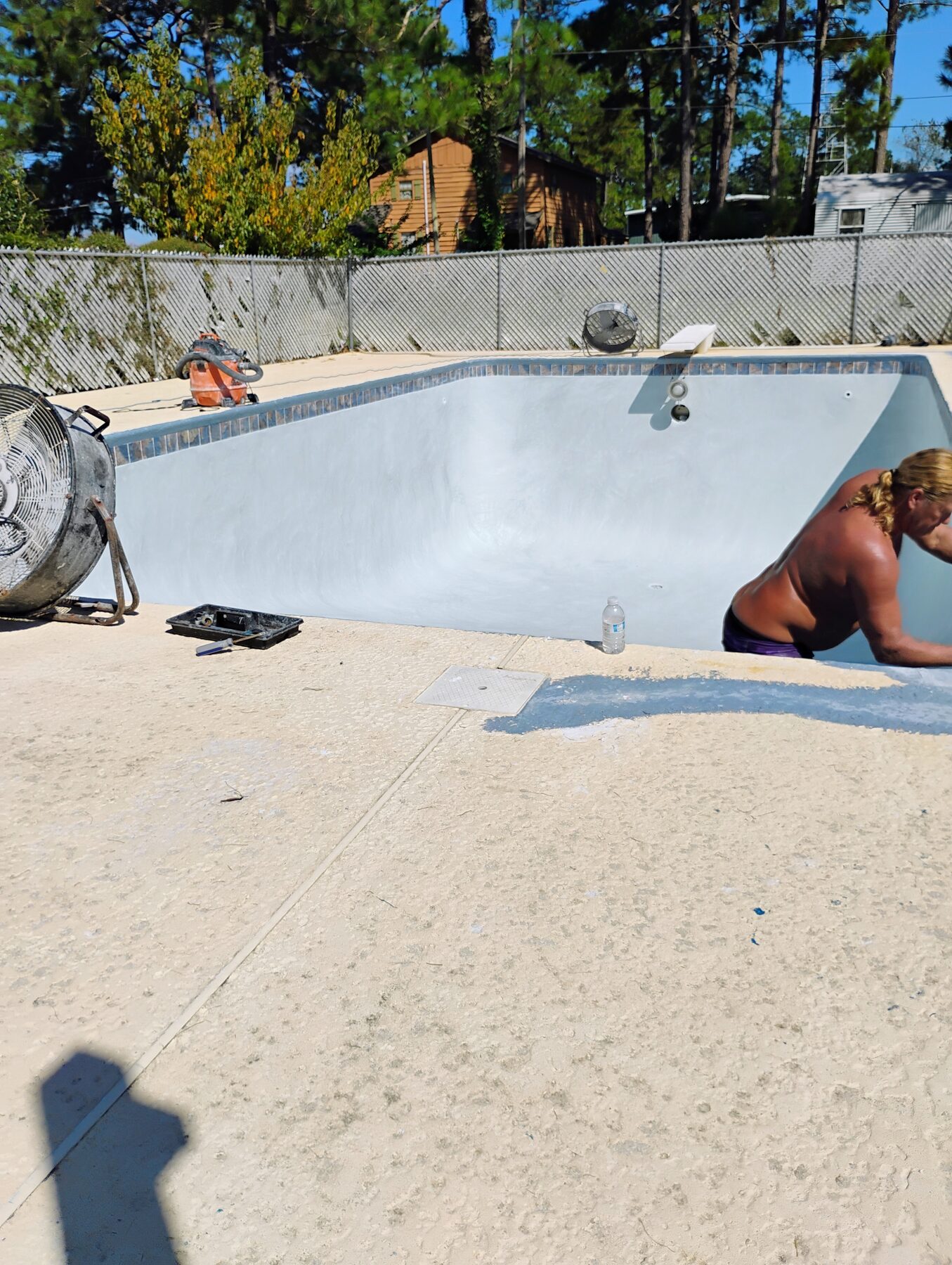 Worker inside an empty residential pool during prep stage with gray plaster and waterline tile in place